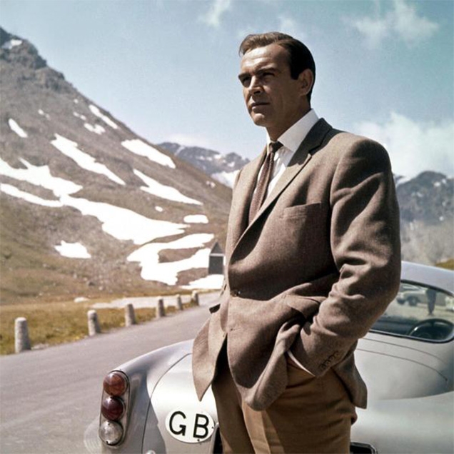 Sean Connery as James Bond wears Anthony Sinclair Barleycorn tweed hacking jacket with Cavalry Twill Trousers during the car chase in Goldfinger.