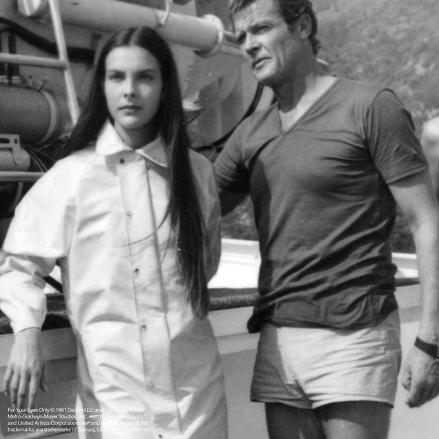 Roger Moore in a behind the scenes photo of For Your Eyes Only wearing a blue v-neck t-shirt and white shorts. The shorts are not seen in the film, he wears long trousers instead.