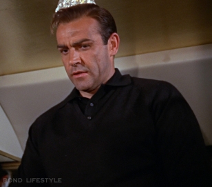 Sean Connery wears a black v-neck sweater over a black polo shirt in Goldfinger
